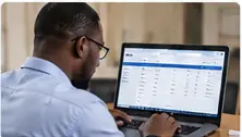 Ghanaian school administrator reviewing existing student records on a laptop